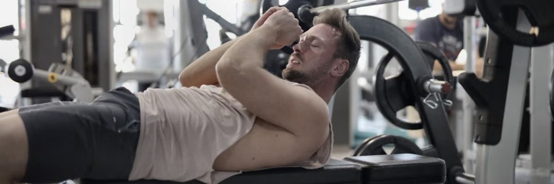 Focused muscular sportsman in modern sportswear preparing to workout with heavy barbell on bench training in modern gym