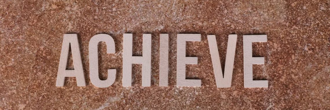 Wooden letters spelling 'ACHIEVE' on a textured brown surface, conveying motivation and success.